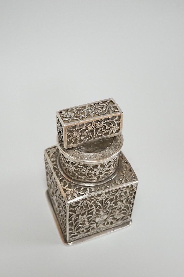 A Persian pierced white metal overlaid moulded glass salts bottle with stopper, decorated with urns and birds amid scrolling foliage, overall height 94mm.